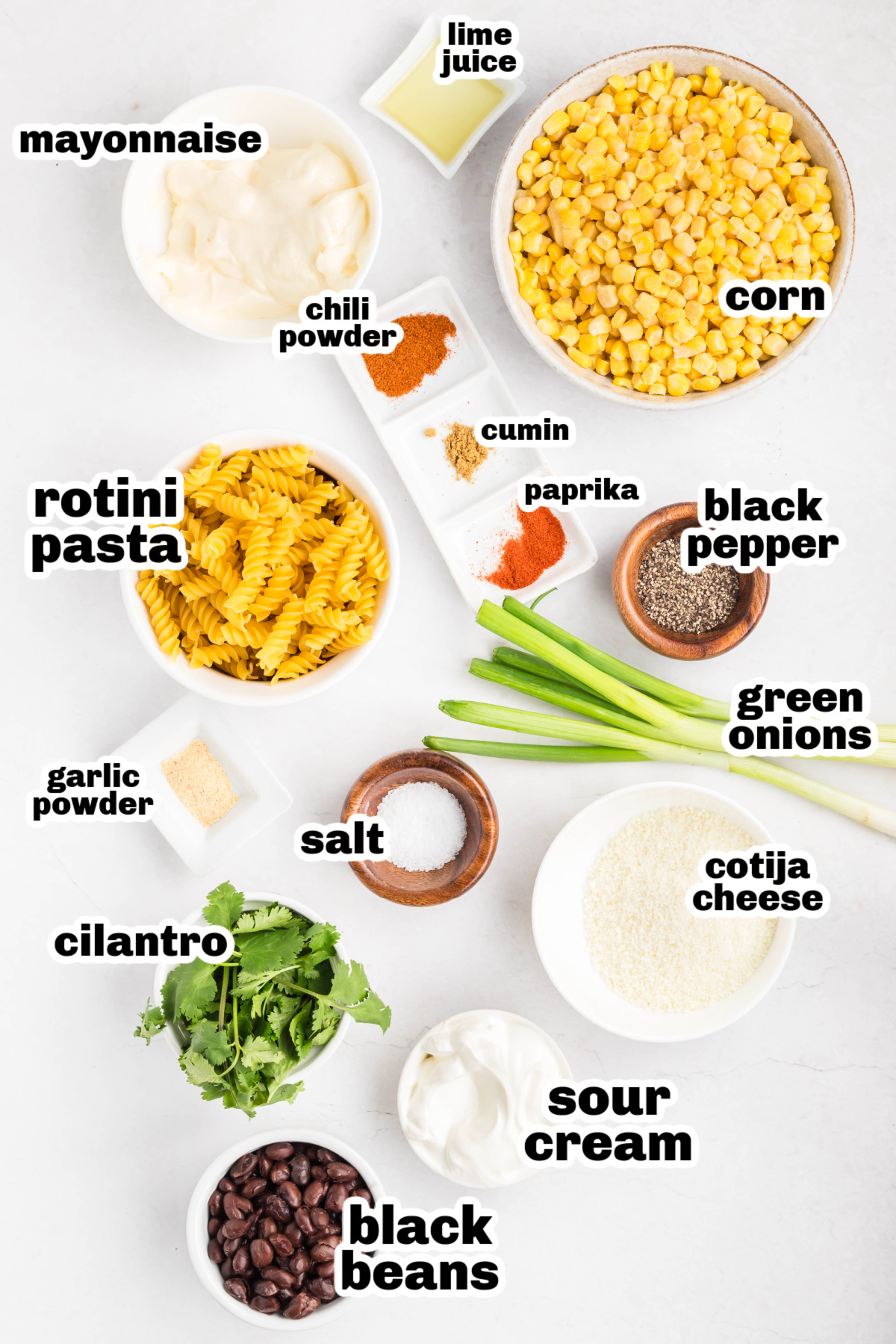 Ingredients for street corn pasta salad including rotini pasta, corn, cotija cheese, cilantro, green onions, black beans, sour cream, mayonnaise, lime juice, and spices
