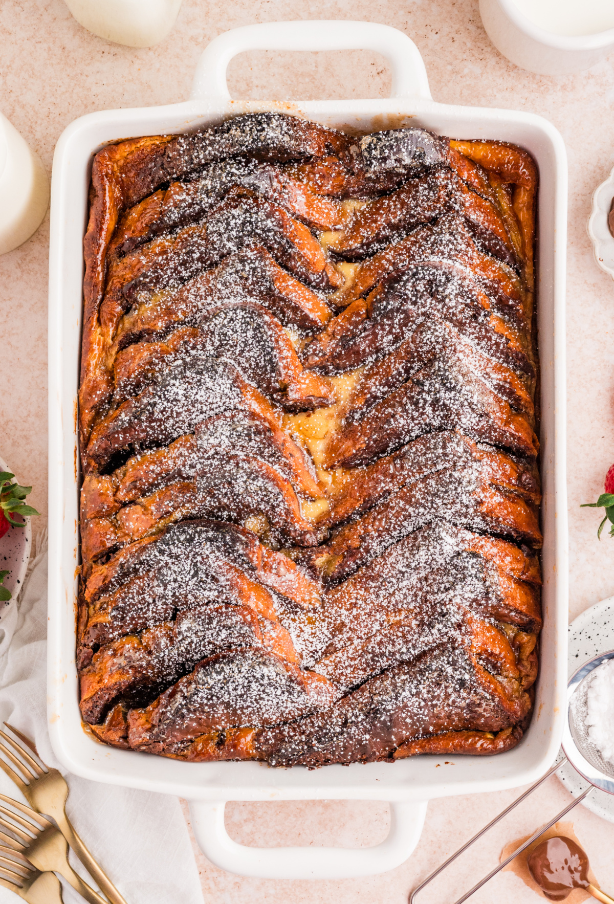 Nutella French Toast Bake in a white baking dish with layered brioche and powdered sugar on top