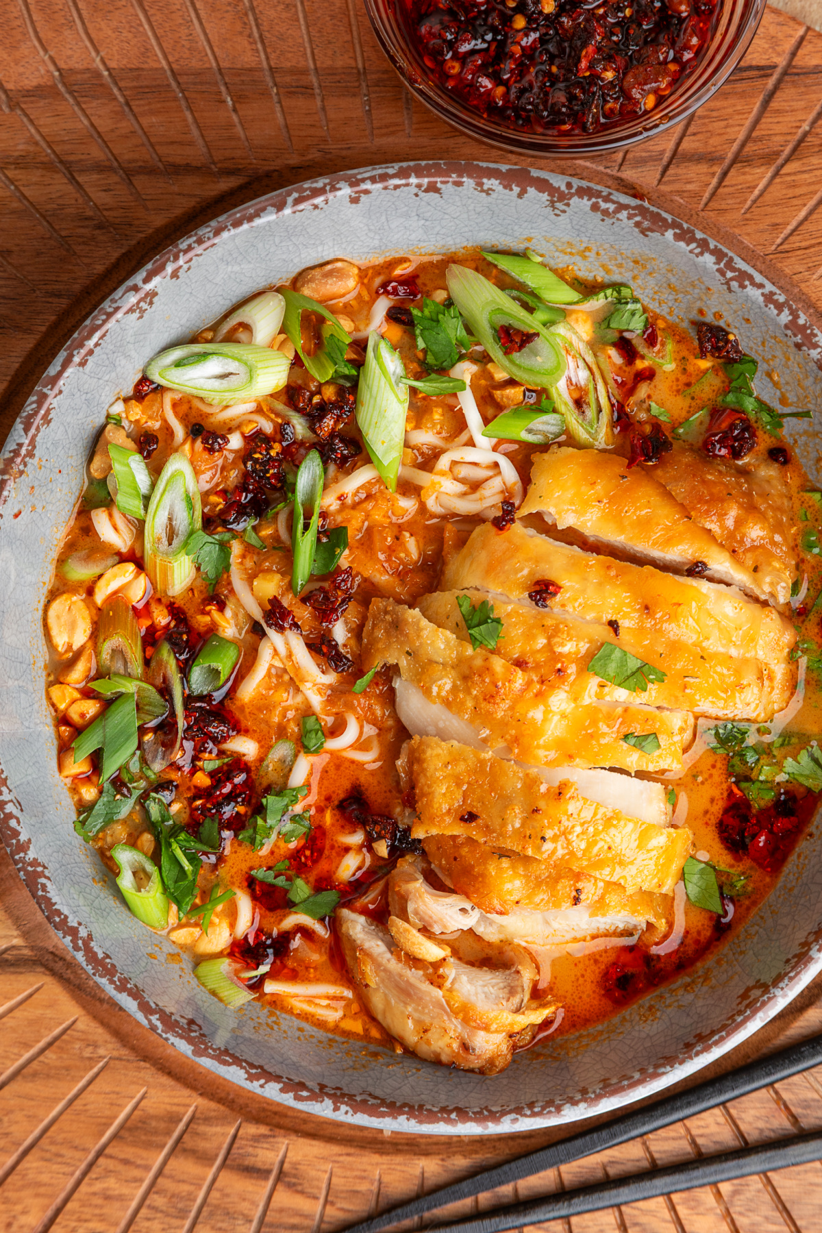 Panang curry ramen topped with sliced crispy chicken thighs, chili crunch, scallions, cilantro, and peanuts