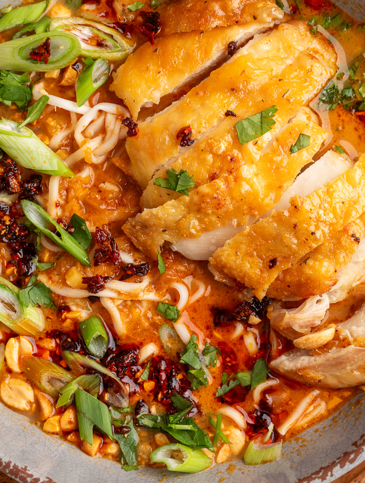 Panang curry ramen with crispy chicken sliced over coconut curry broth, ramen noodles, chili crunch, scallions, cilantro, and peanuts