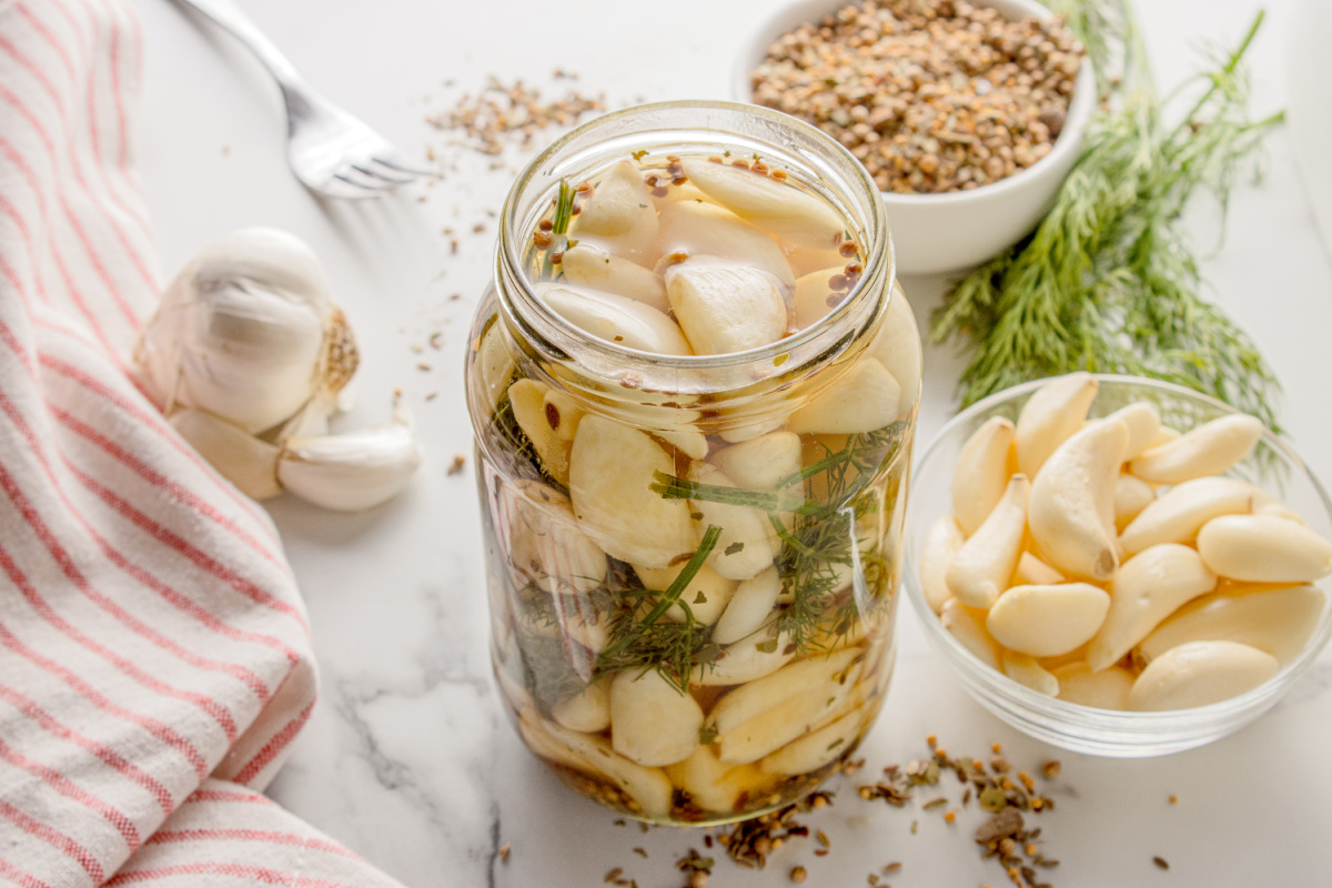 Overhead view of Pickled Dill Garlic with fresh cloves, dill, and pickling spice