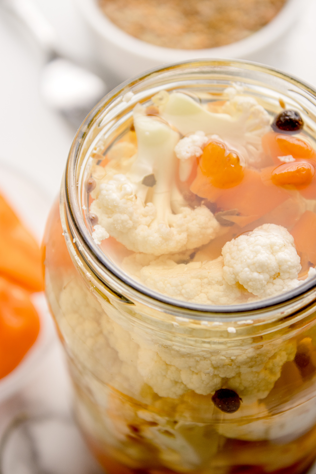 Close-up of spicy pickled cauliflower florets and habanero slices submerged in clear vinegar brine