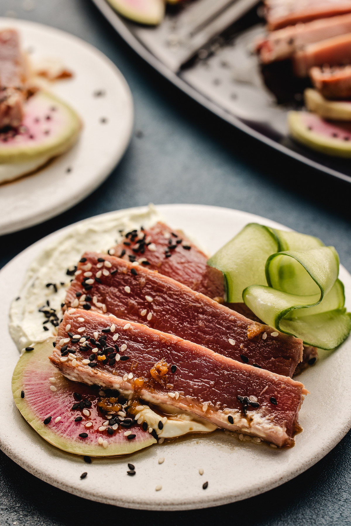 Rare ahi tuna slices with sesame seeds, cucumber ribbons, and watermelon radish over wasabi yogurt