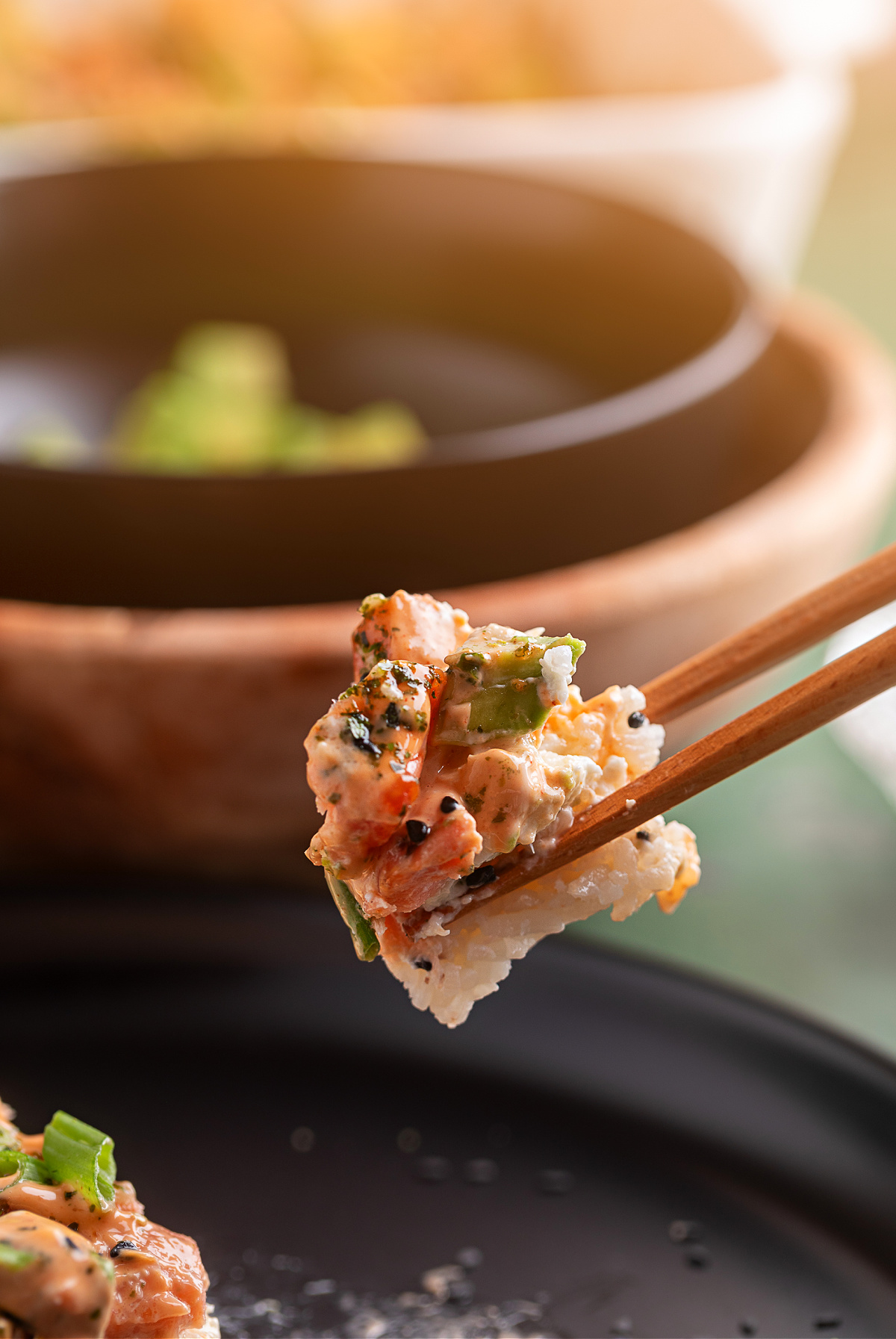 Salmon Crab Sushi Bake bite held with chopsticks showing rice, crab, salmon, and spicy mayo