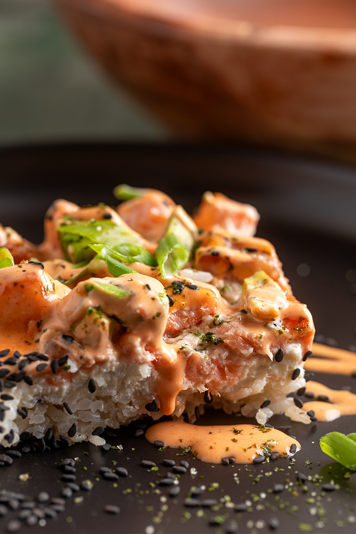 Salmon Crab Sushi Bake slice layered with jasmine rice, creamy crab, baked salmon, and spicy mayo on a dark plate
