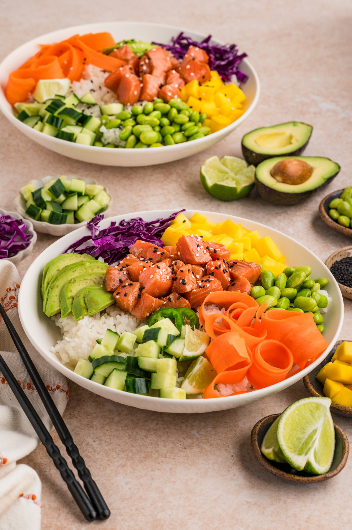 Two salmon poke bowls with sushi rice, mango, avocado, edamame, cucumber, and marinated salmon