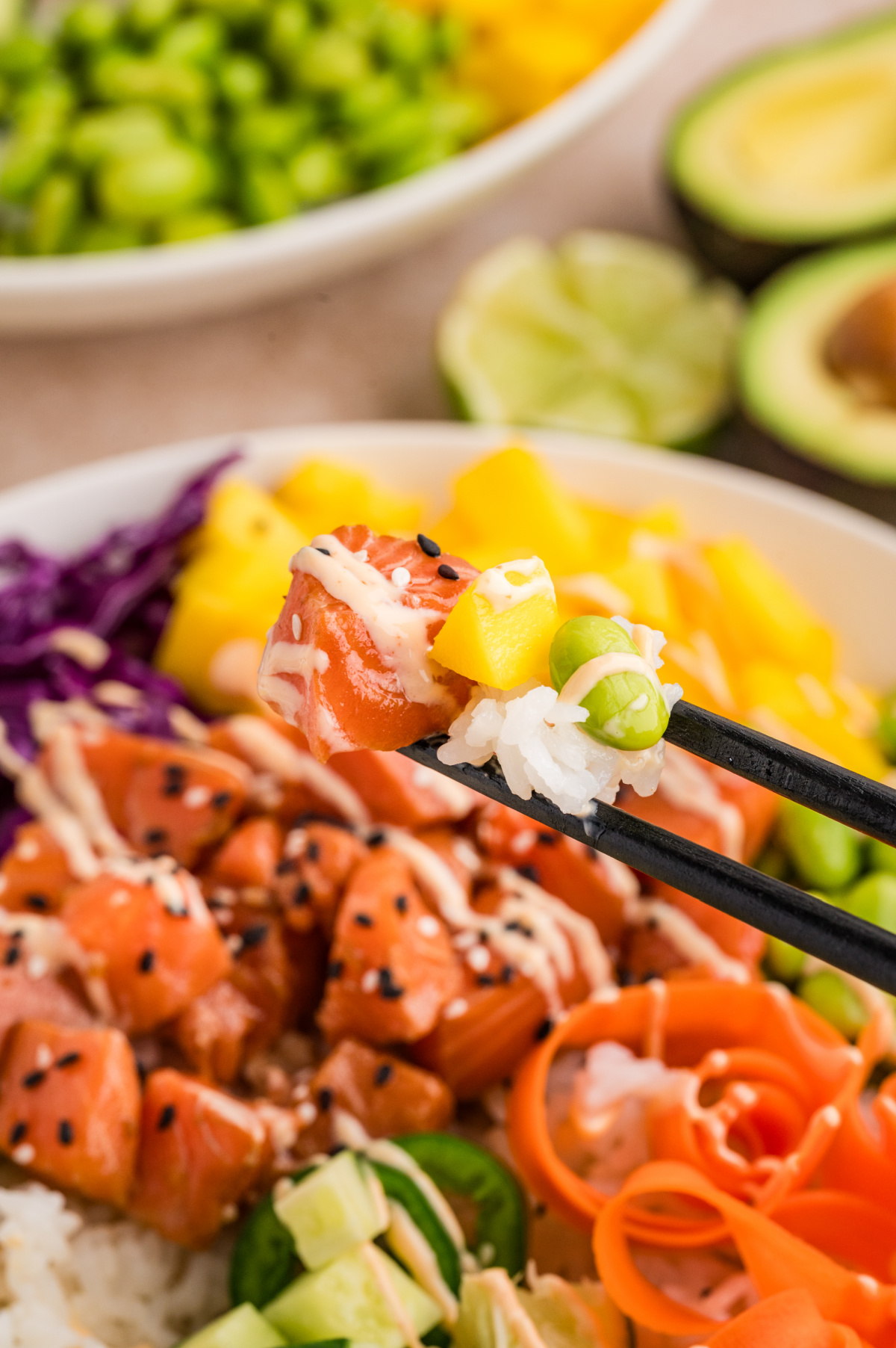 Salmon poke bowls bite with marinated salmon, sushi rice, mango, and edamame held with chopsticks
