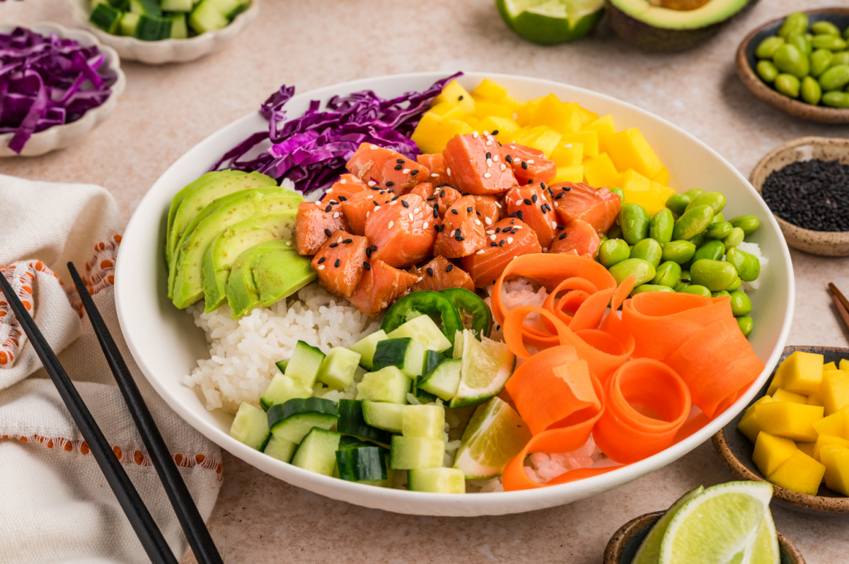 Salmon poke bowl with sushi rice, mango, avocado, edamame, cucumber, and shredded carrots