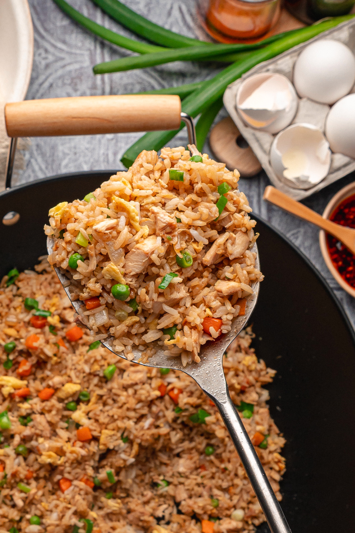 Chicken fried rice cooked in a wok with rotisserie chicken, eggs, peas, carrots, and green onions