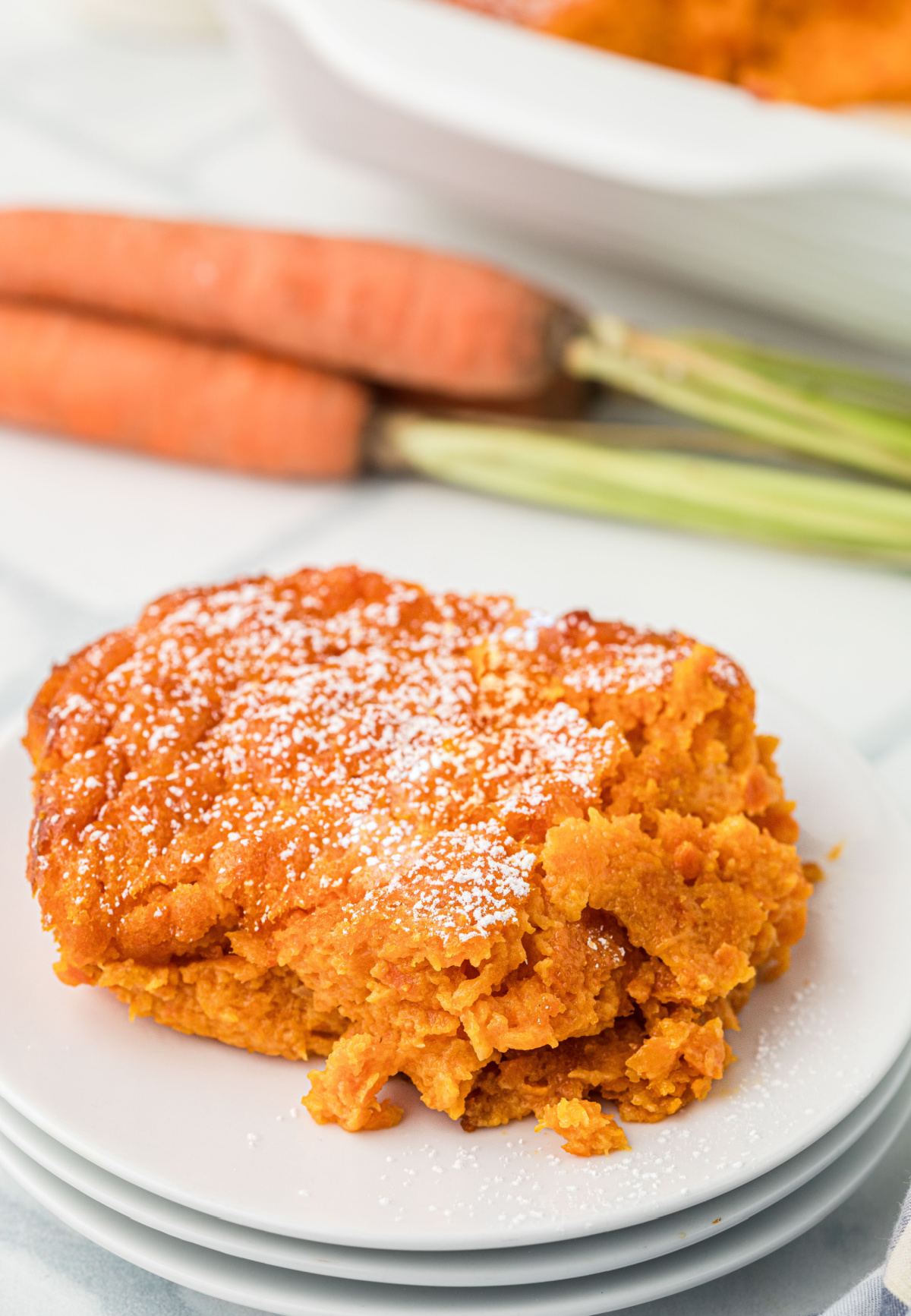Slice of sweet carrot casserole dusted with powdered sugar on white plate