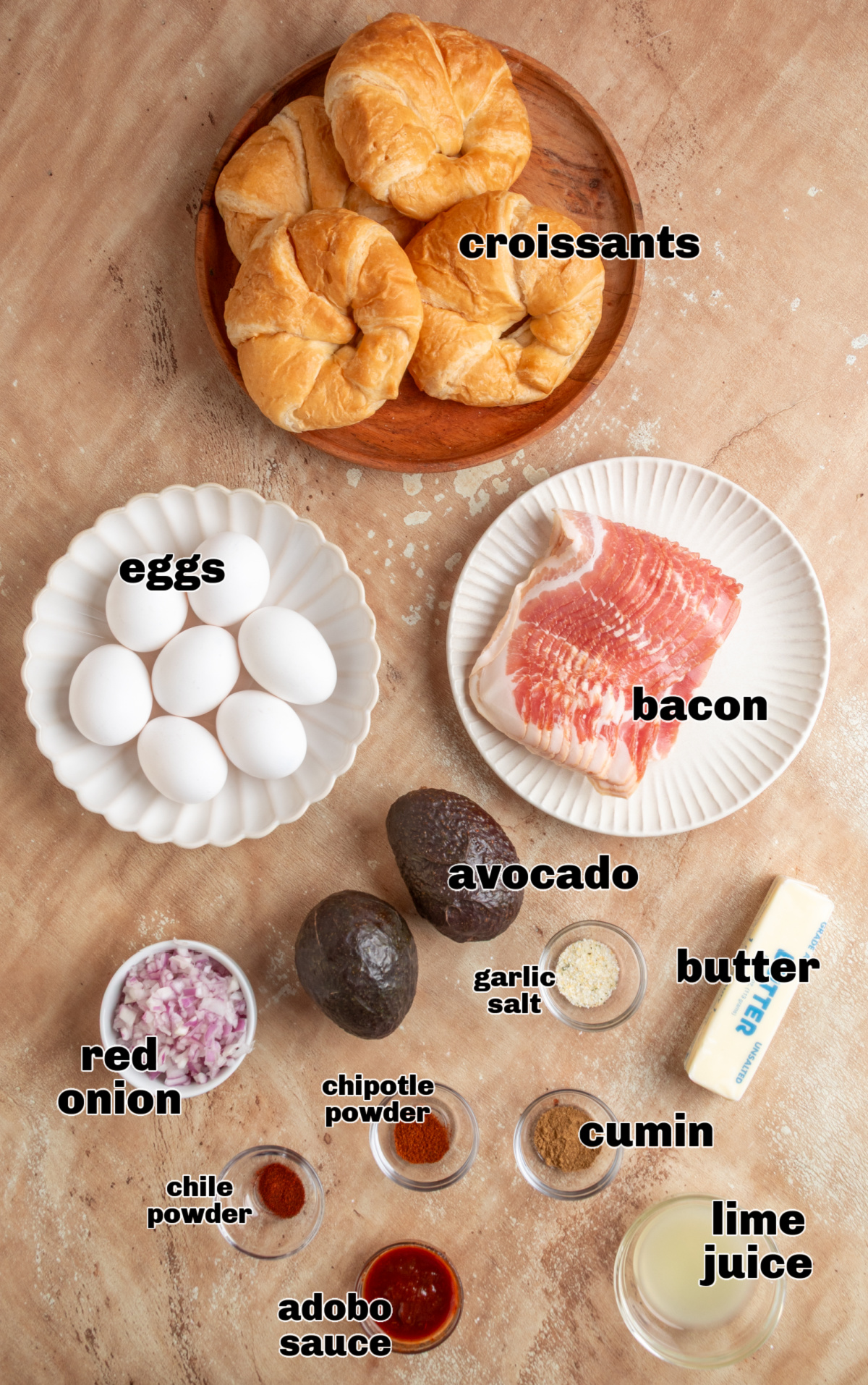 Ingredients for croissant breakfast sandwich including eggs, bacon, avocado, red onion, adobo sauce, chipotle powder and lime juice
