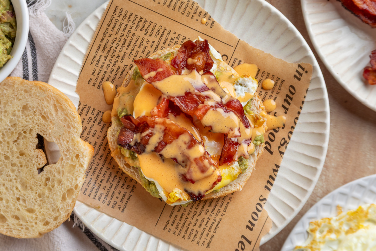 Overhead view of a bacon egg avocado breakfast sandwich layered with mashed avocado, crispy bacon, sunny side egg and chipotle hollandaise on a croissant