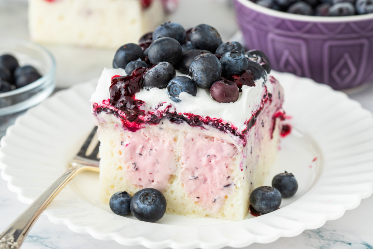 Slice of blueberry cheesecake poke cake showing creamy filling and blueberry layers