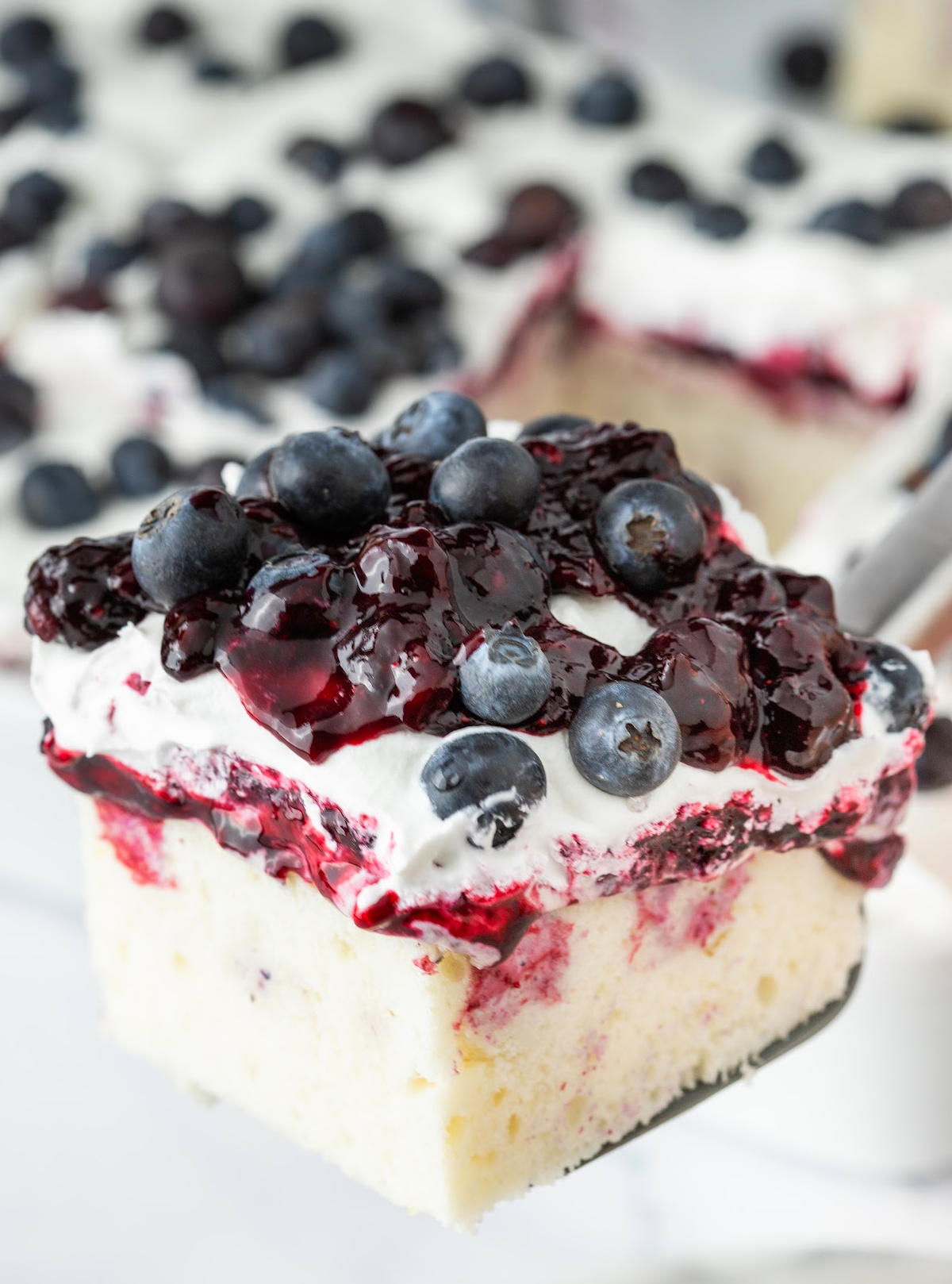 Slice of blueberry cheesecake poke cake with blueberry compote and whipped topping