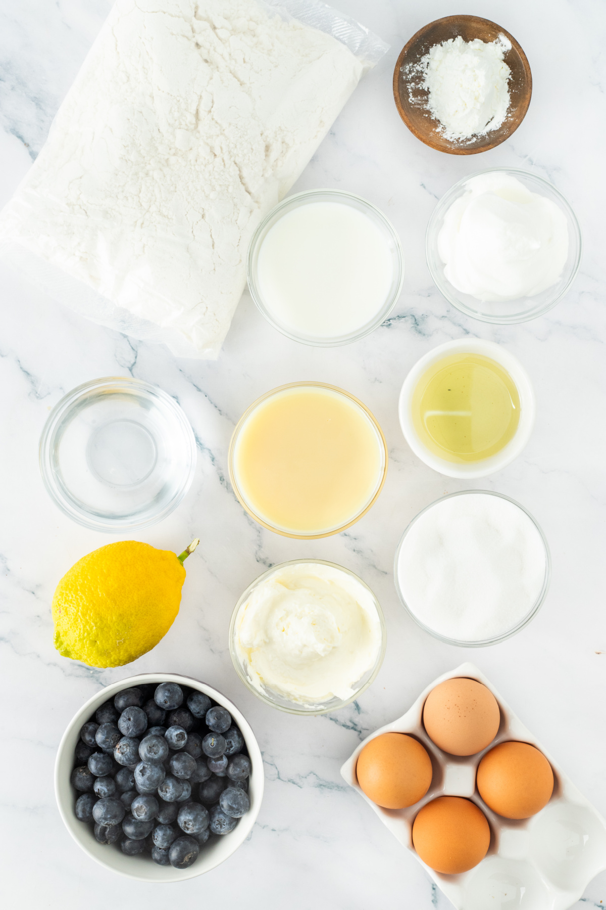 Ingredients for blueberry poke cake including cake mix, blueberries, cream cheese, eggs, and lemon