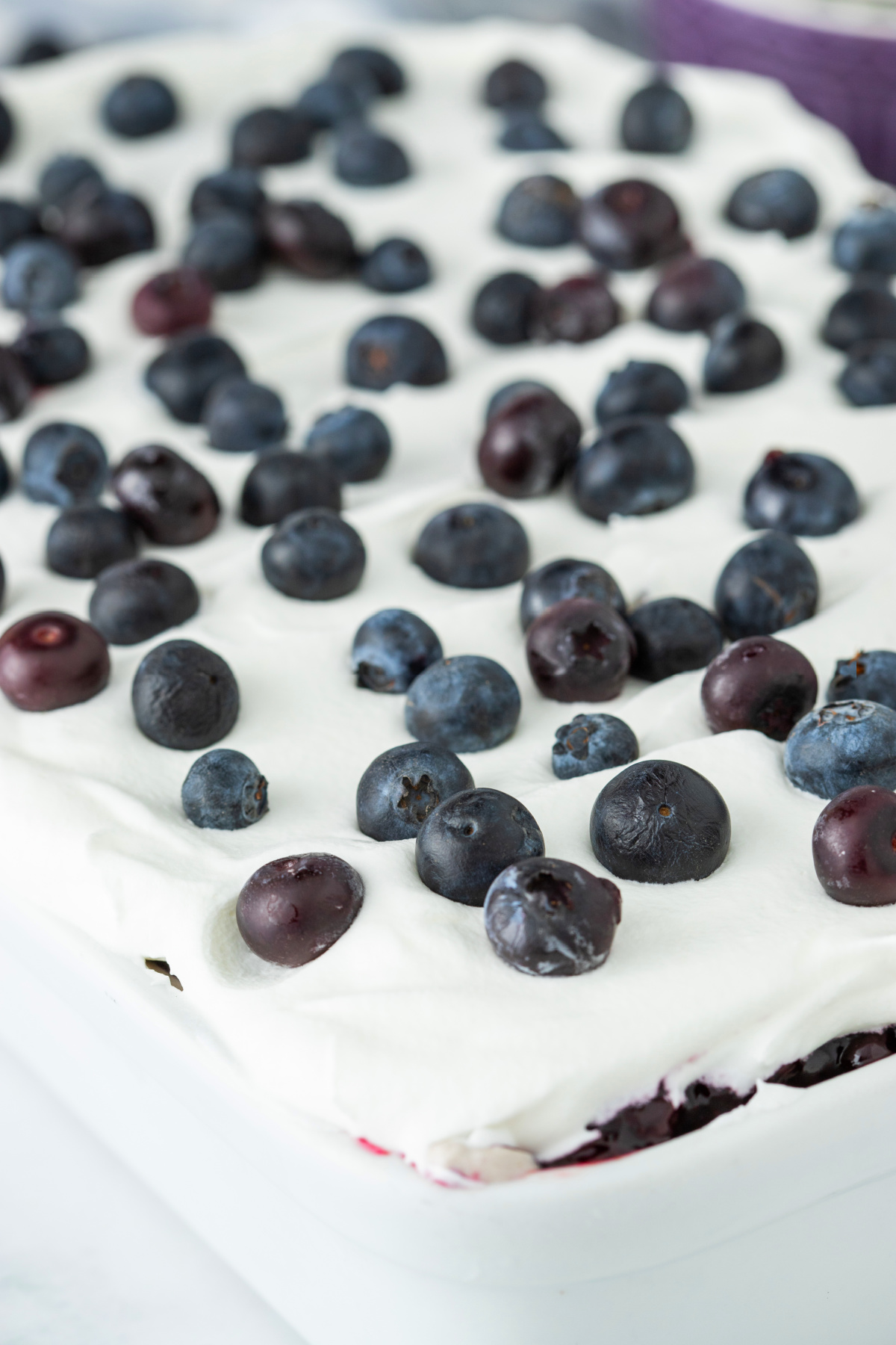 Blueberry poke cake topped with whipped topping and fresh blueberries in a baking dish