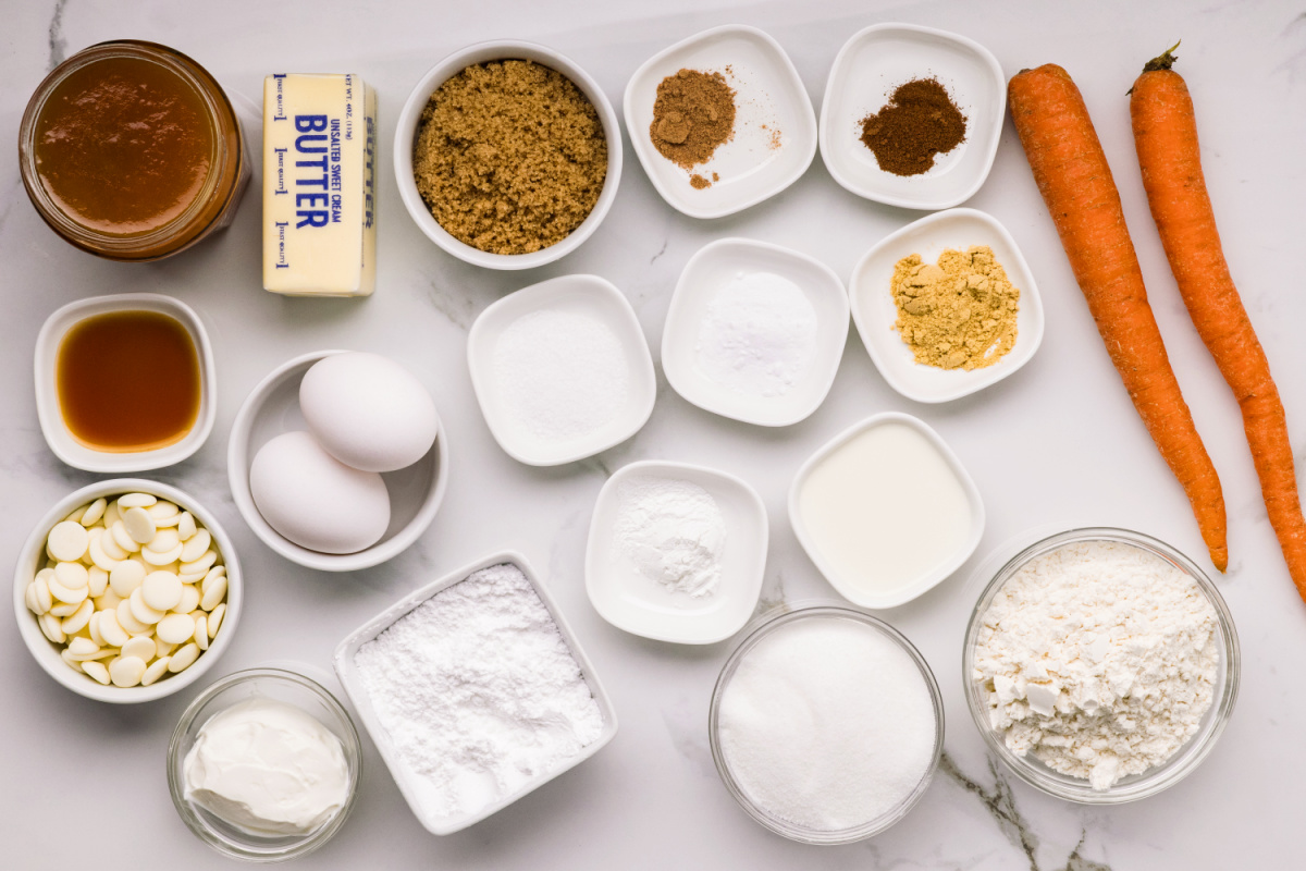 Ingredients for carrot cake with apricot filling including fresh carrots, flour, sugar, spices, sour cream, butter, eggs, and white chocolate