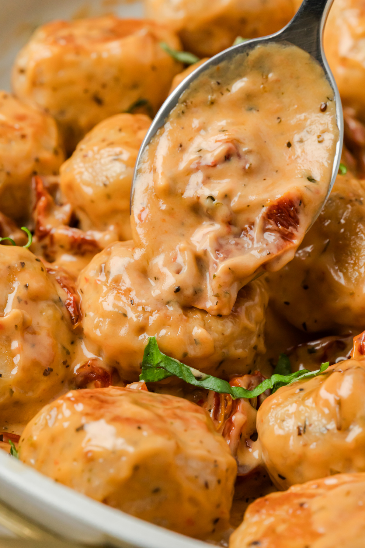 Spoon lifting creamy sun-dried tomato Parmesan sauce over tender chicken meatballs in a skillet