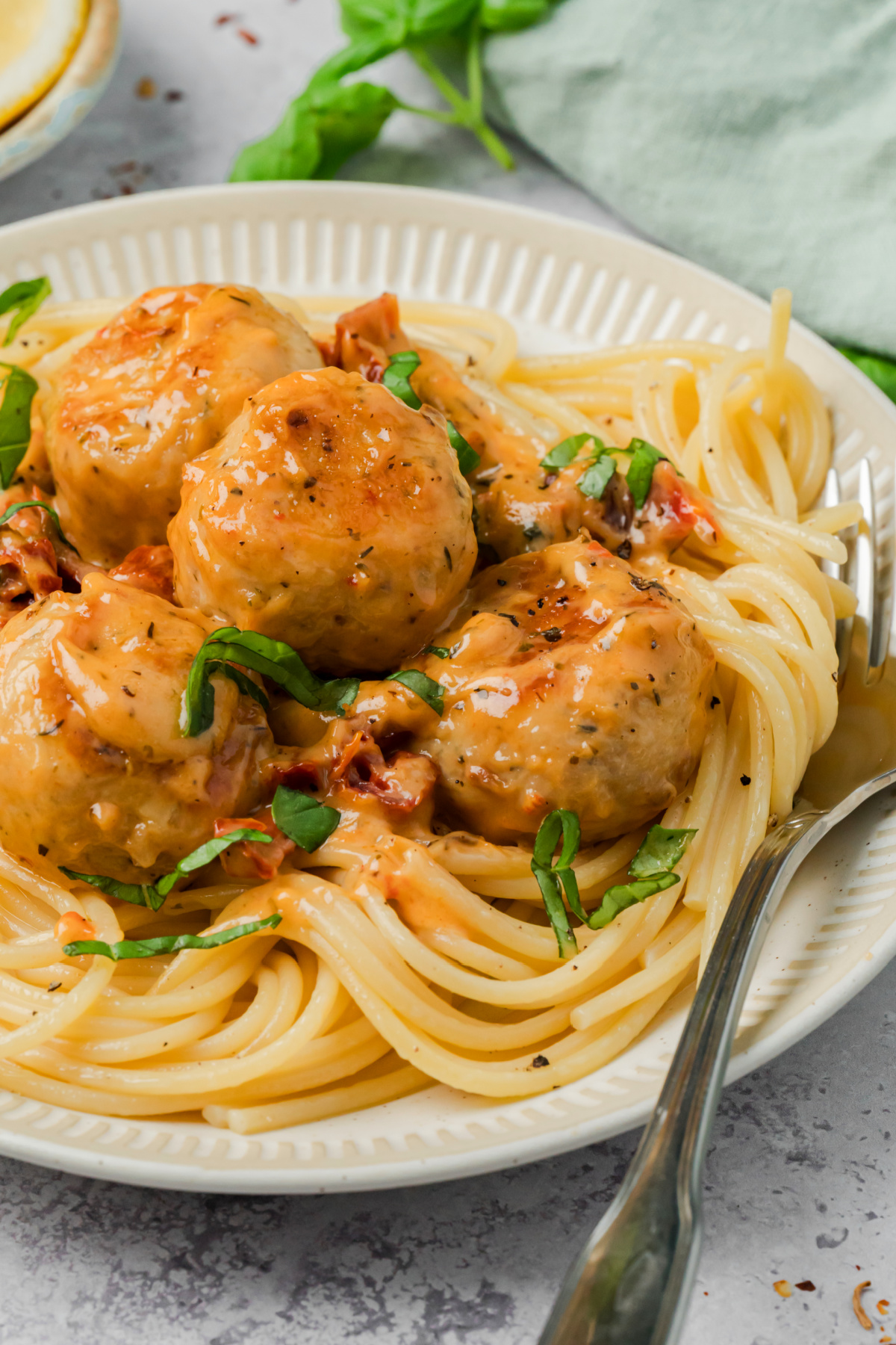 Creamy chicken meatballs with sun-dried tomato sauce served over spaghetti and topped with fresh basil