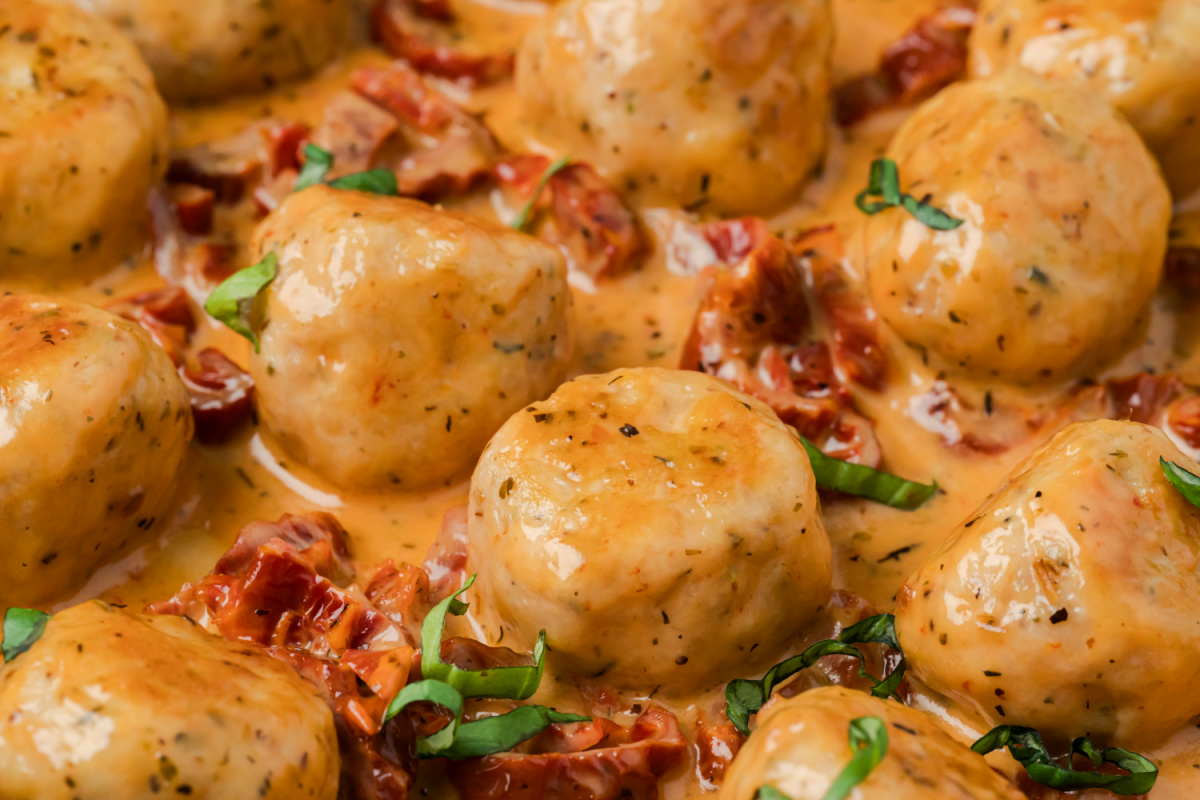 Close-up of creamy chicken meatballs simmered in sun-dried tomato Parmesan sauce with fresh basil