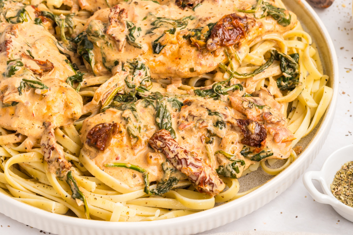 creamy tuscan chicken over pasta with sun-dried tomatoes, spinach, and parmesan sauce