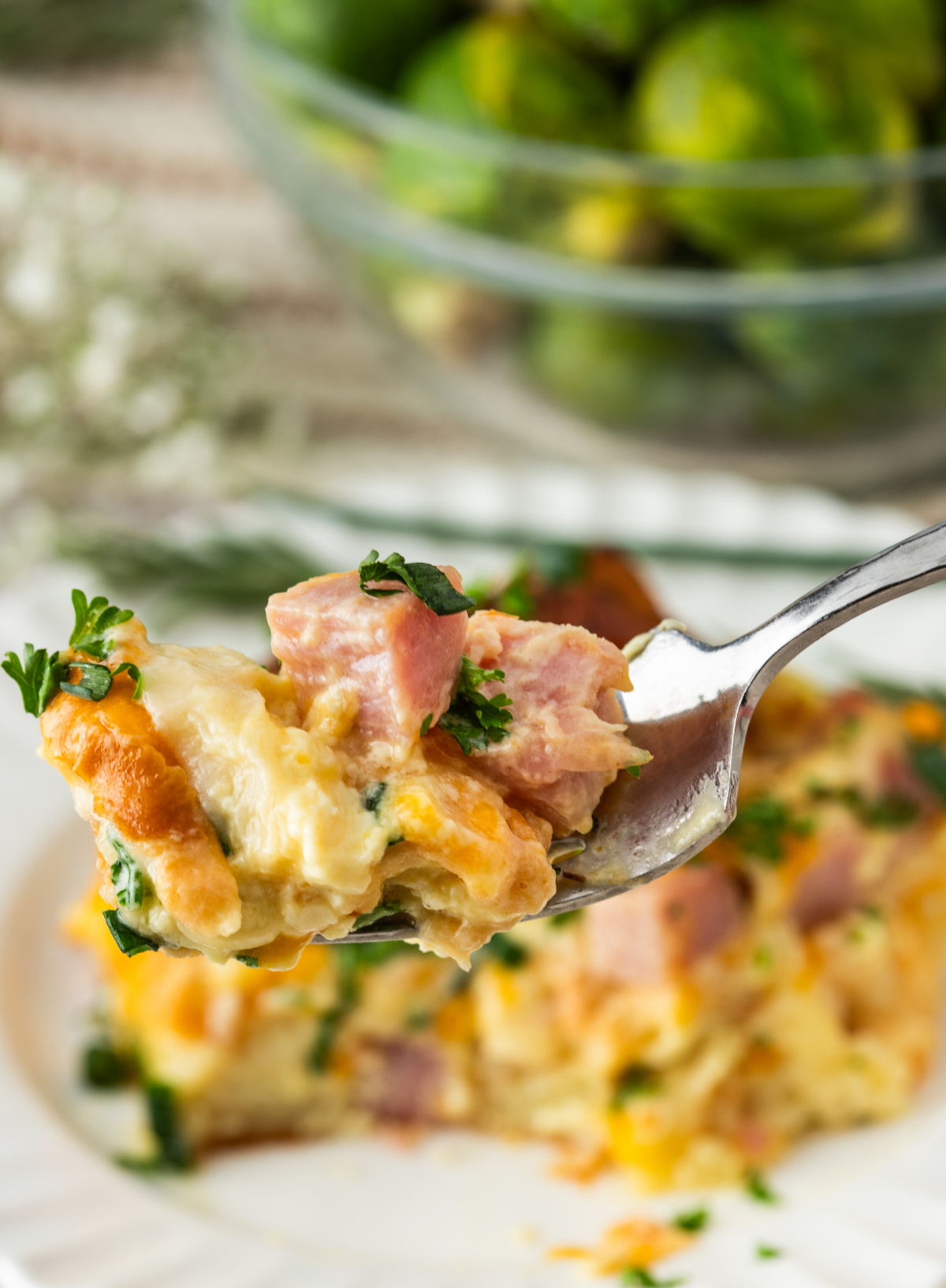 forkful of croissant breakfast bake with ham, melted cheese, egg custard, and fresh herbs