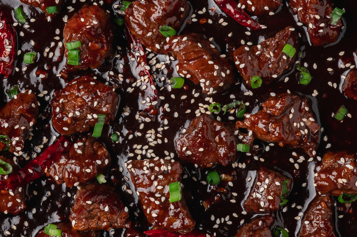 close up of gochujang steak bites in skillet with sesame seeds and green onions