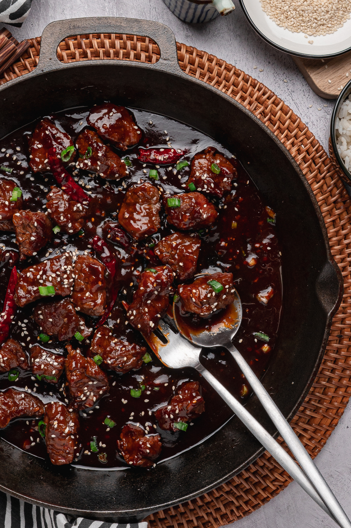 gochujang steak bites in skillet with sesame seeds green onions and dried chiles