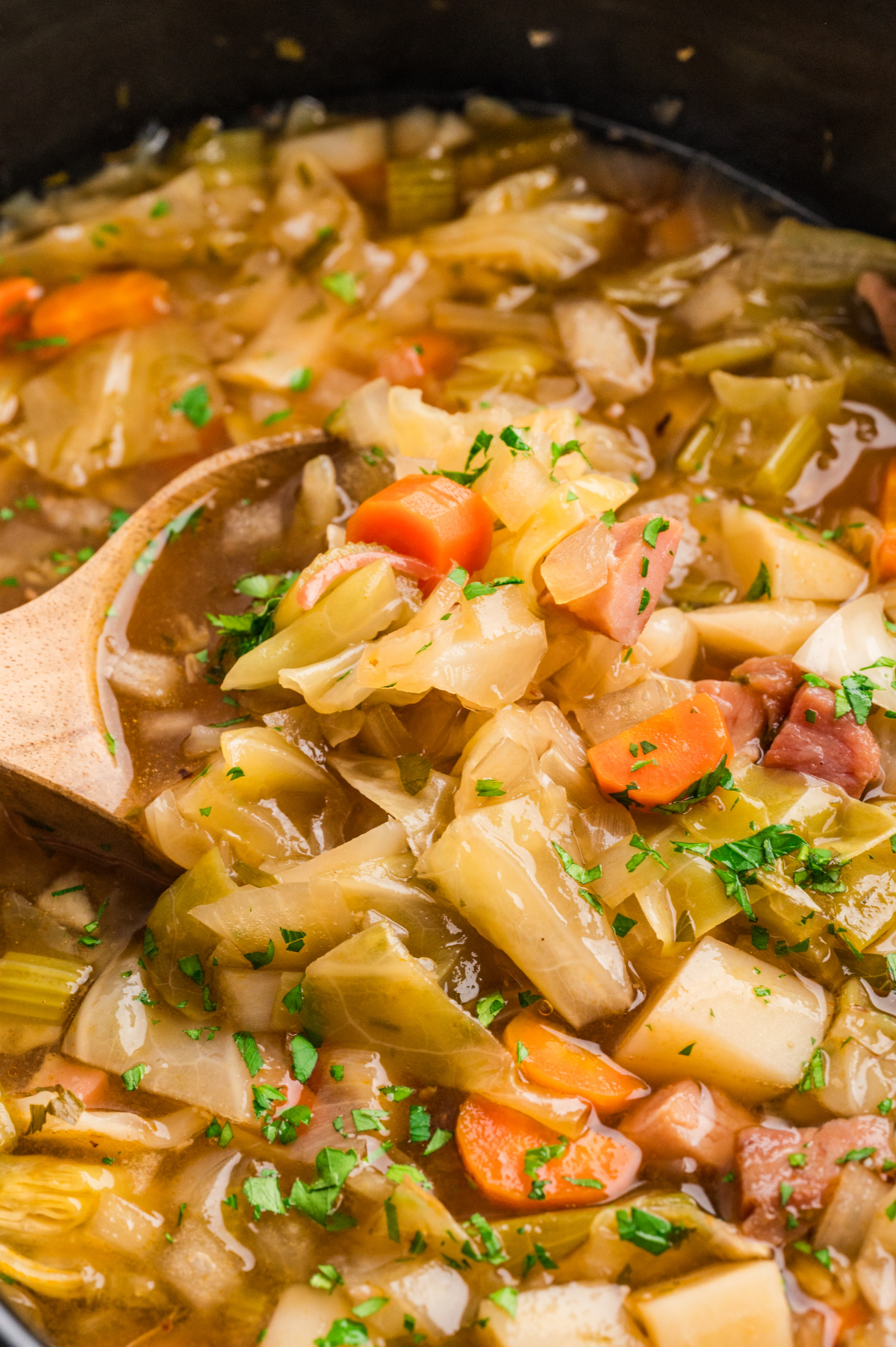 Ham cabbage soup cooking in a slow cooker with cabbage, potatoes, carrots, and ham in broth