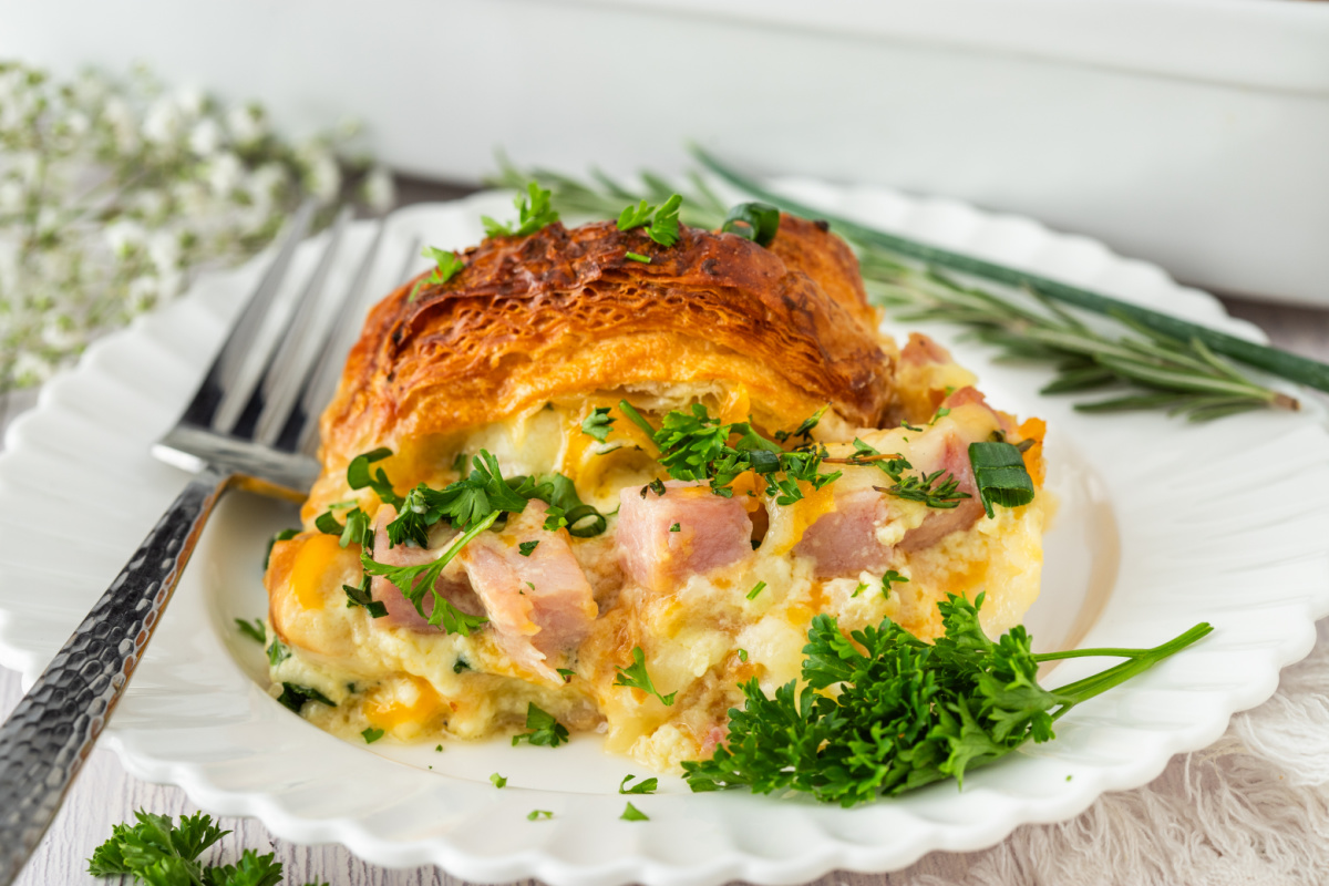 slice of ham and cheese croissant breakfast bake served on a white plate with parsley and chives