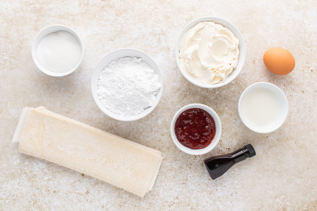 ingredients for strawberry cream cheese danishes including puff pastry, cream cheese, strawberry jam, sugar, and egg