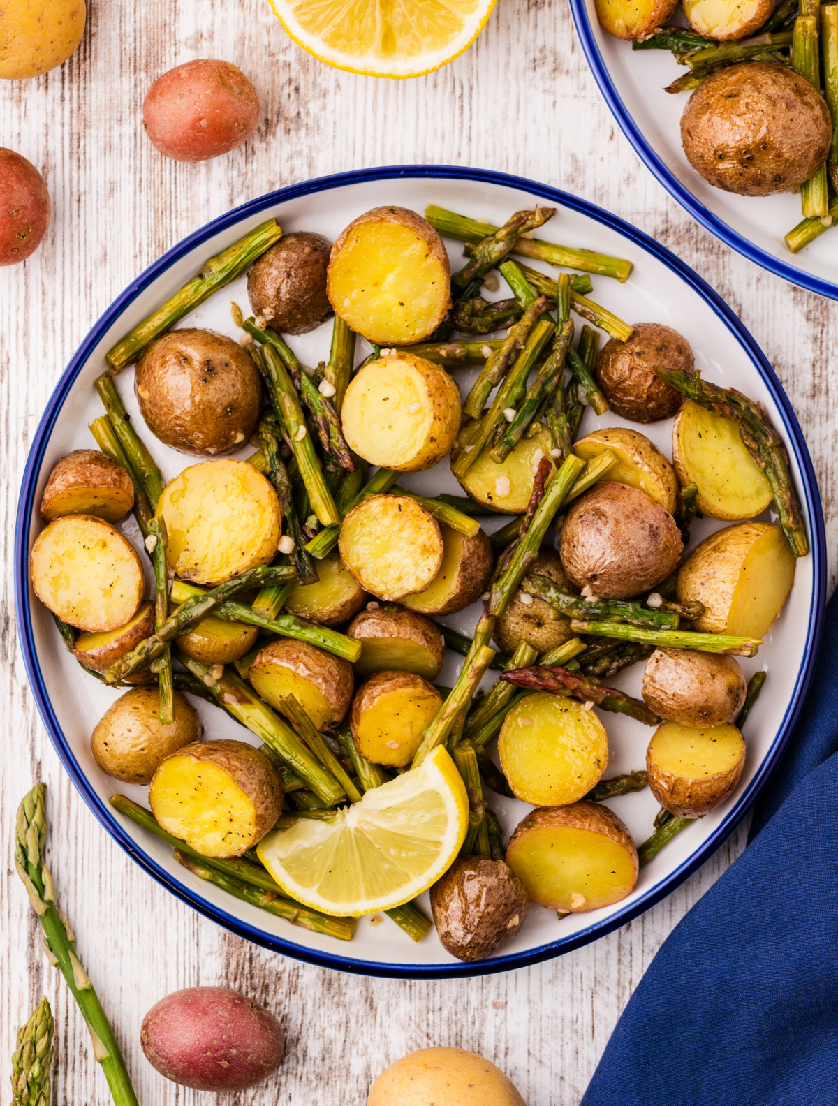lemon garlic roasted potatoes and asparagus plated with lemon wedge, golden potatoes and tender asparagus on white plate