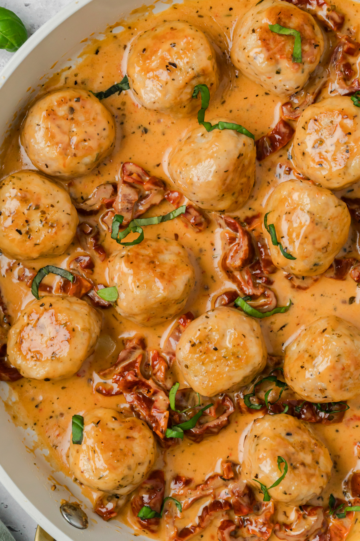 Marry me chicken meatballs in a creamy sun-dried tomato Parmesan sauce, garnished with fresh basil in a white skillet