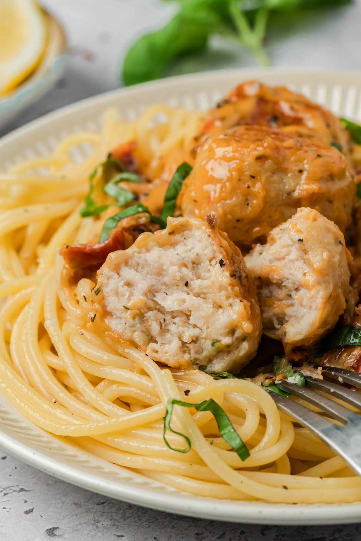 Creamy chicken meatballs with sun-dried tomato sauce served over spaghetti and topped with fresh basil
