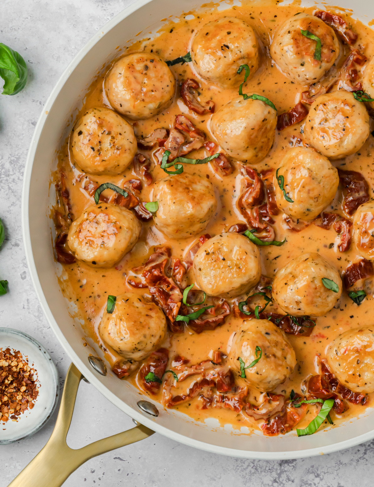 Overhead view of marry me chicken meatballs in a creamy sun-dried tomato sauce with fresh basil and lemon wedges
