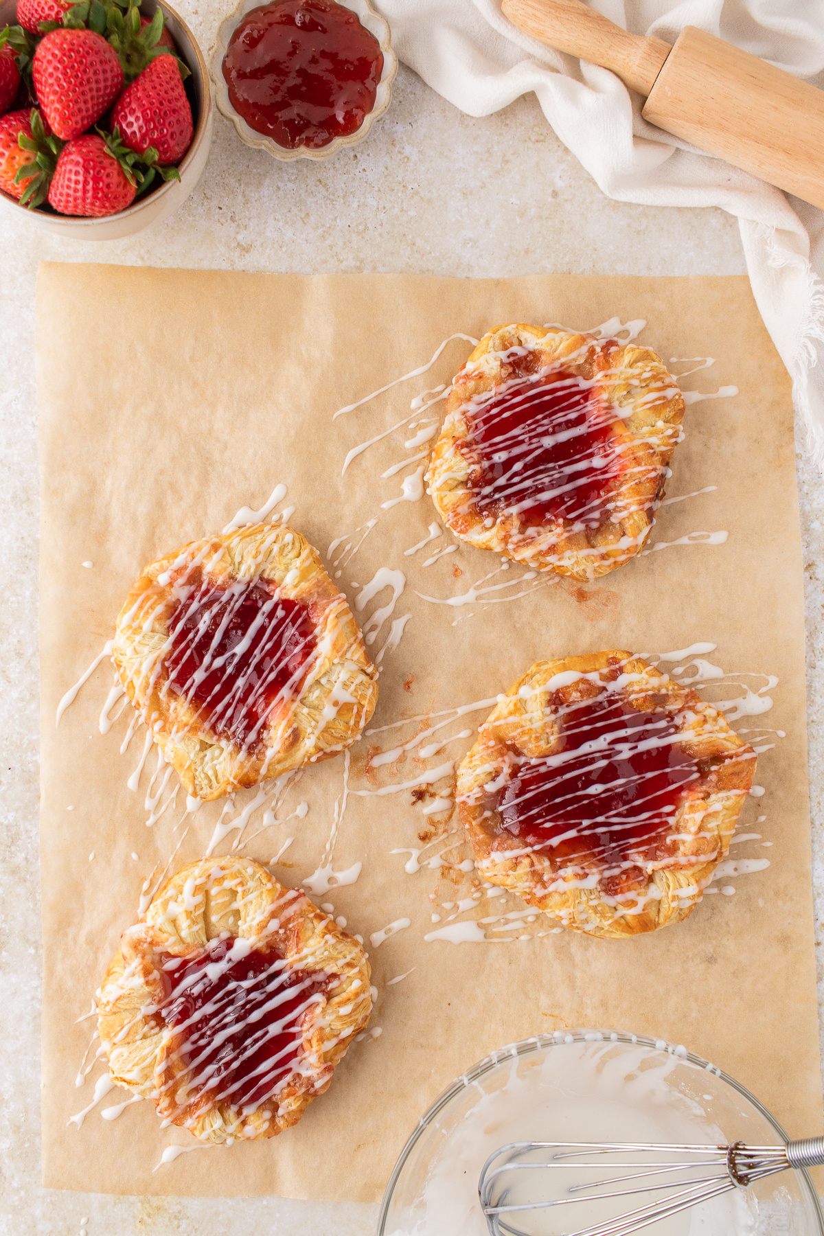 strawberry danish with puff pastry and cream cheese filling topped with jam and glaze on parchment