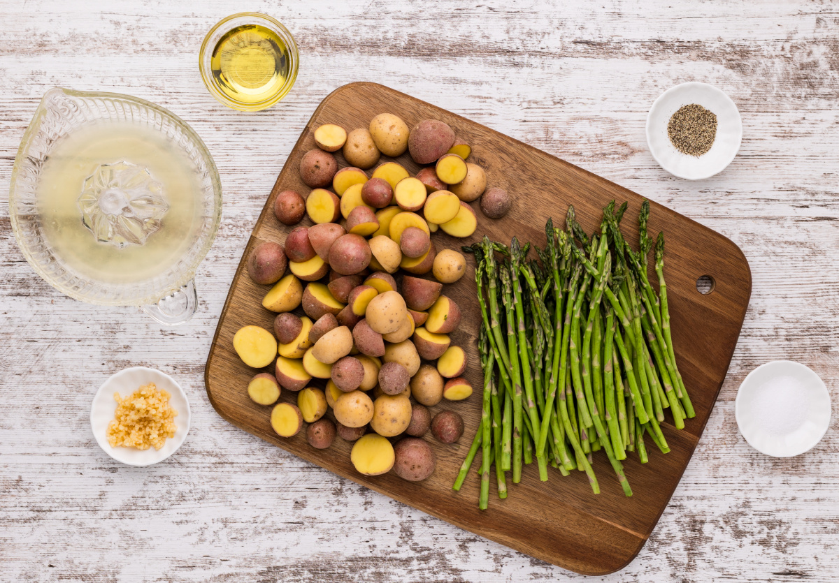 roasted potatoes and asparagus ingredients with baby potatoes, fresh asparagus, lemon juice, garlic, olive oil, salt and pepper on cutting board