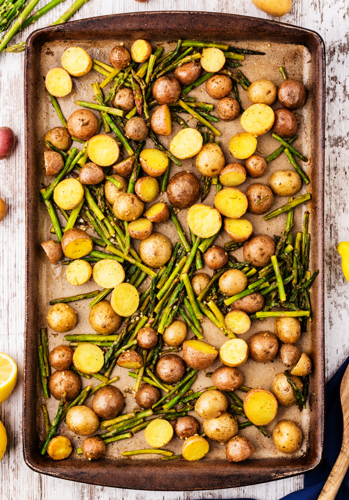 roasted potatoes and asparagus on a sheet pan with lemon and garlic, showing golden halved baby potatoes and roasted asparagus pieces spread in a single layer