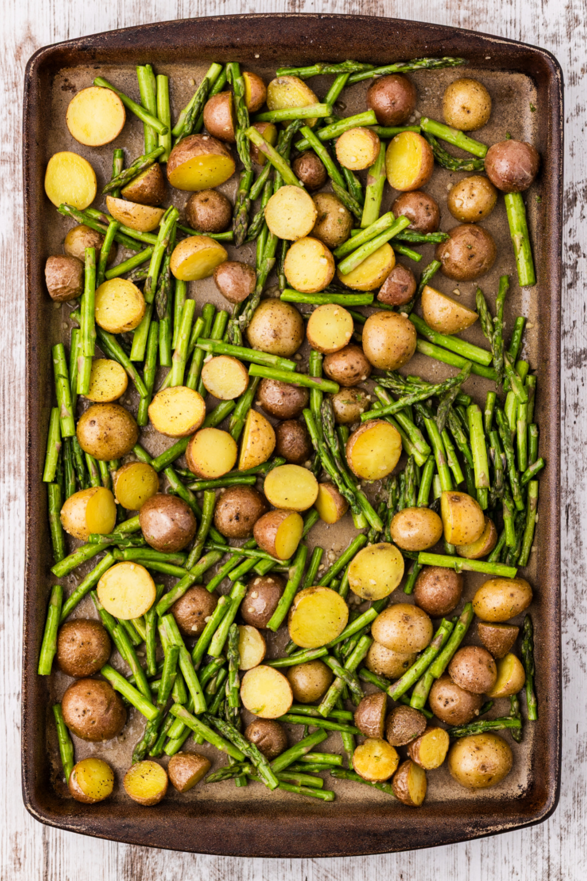 roasted potatoes and asparagus spread in a single layer on sheet pan, showing halved baby potatoes and crisp-tender asparagus