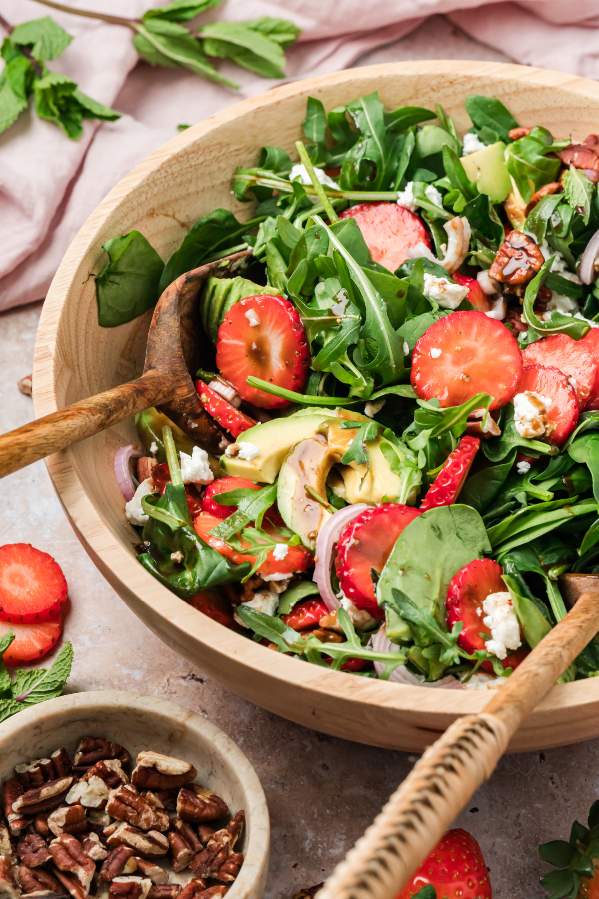 Strawberry goat cheese salad with avocado, pecans, and balsamic vinaigrette in a wooden bowl with spinach and arugula