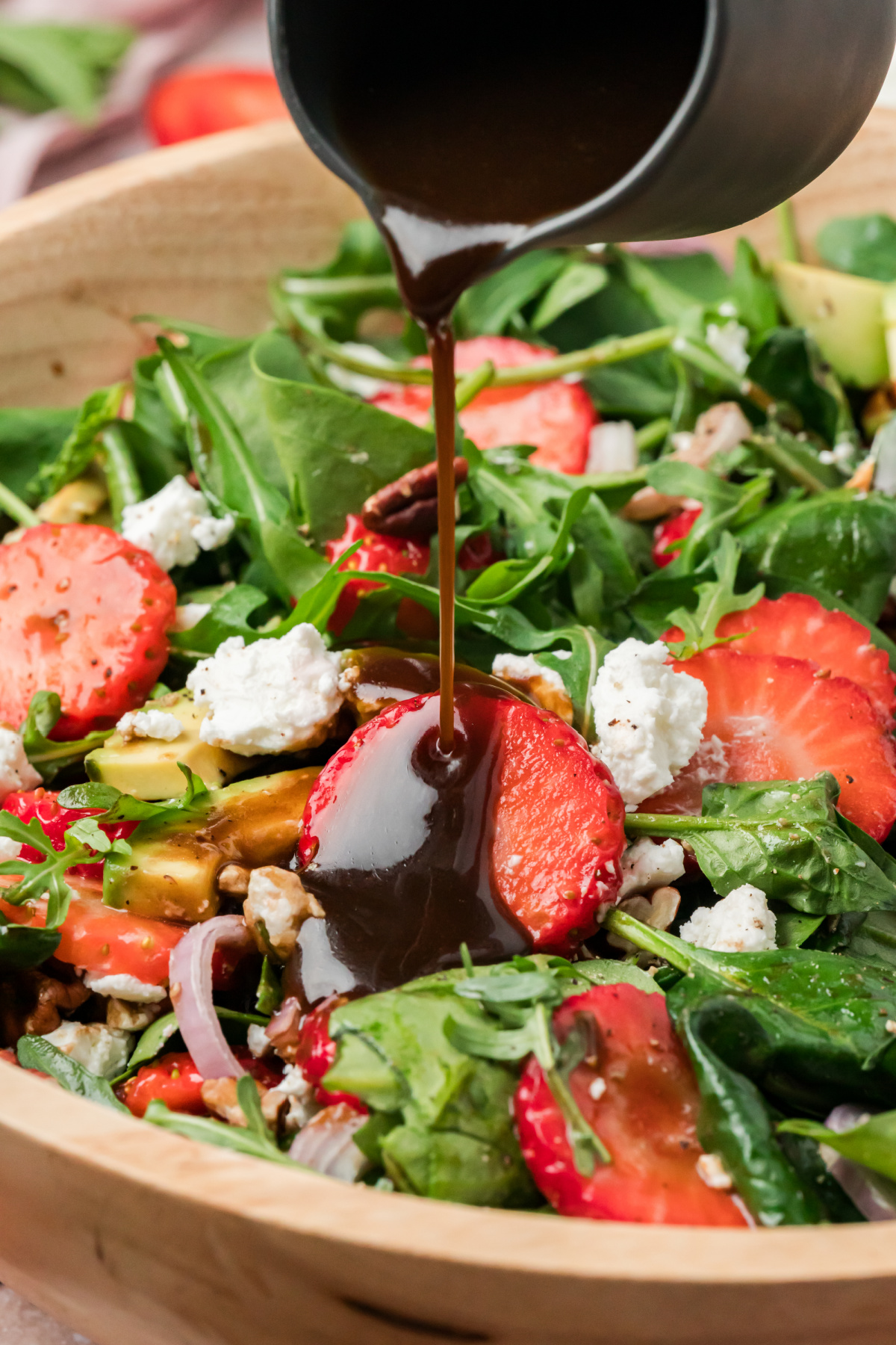 Strawberry goat cheese salad with avocado, pecans, and greens as balsamic vinaigrette is poured over the top