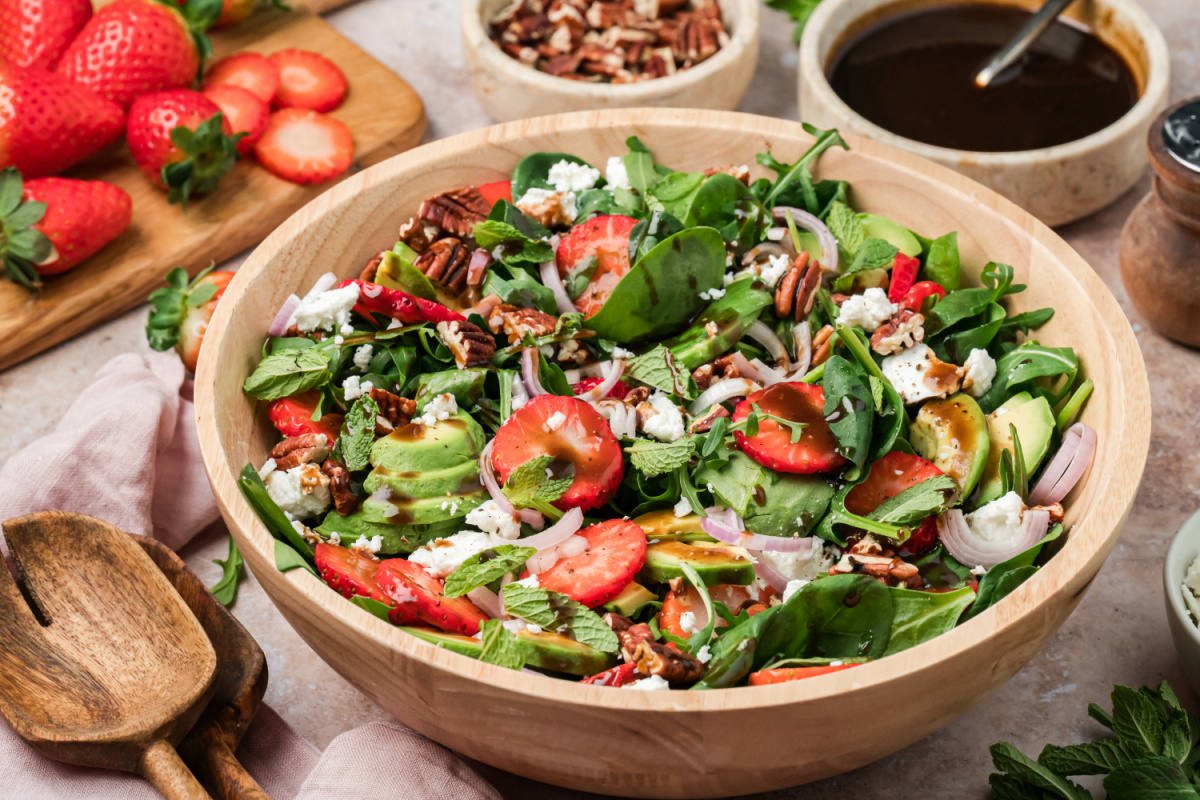 Strawberry spinach goat cheese salad with avocado, toasted pecans, and balsamic vinaigrette in a wooden bowl