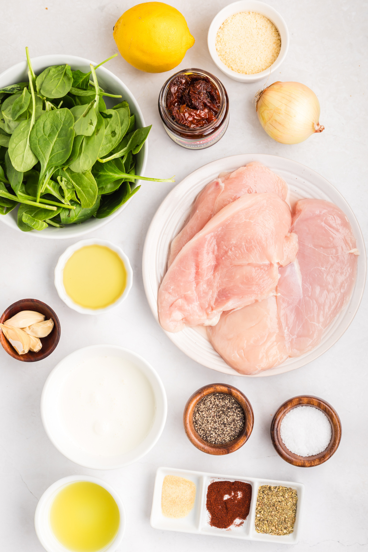 ingredients for tuscan chicken including chicken breasts, spinach, sun-dried tomatoes, garlic, lemon, and parmesan