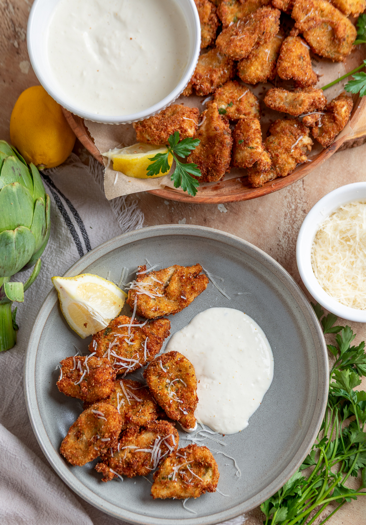 Breaded artichoke hearts with lemon garlic aioli served on plates with lemon wedges and Parmesan