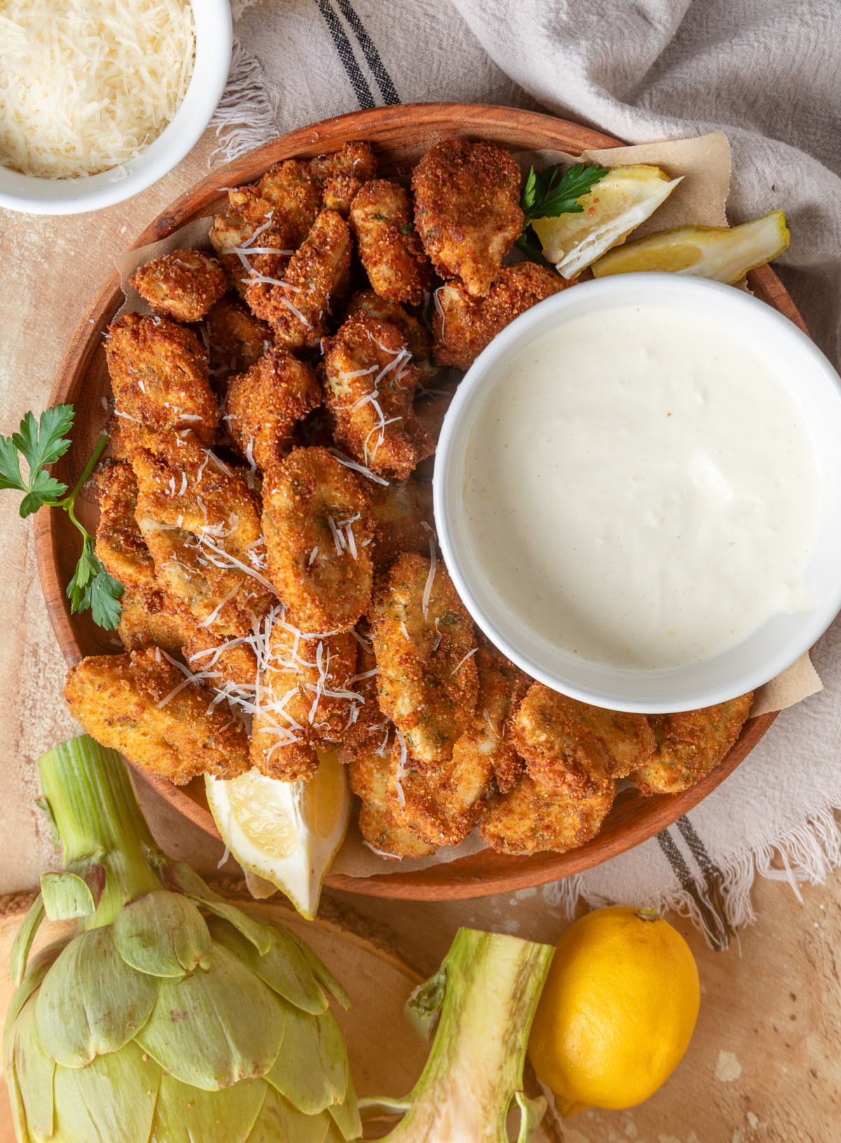 Breaded artichoke hearts served with lemon garlic aioli, lemon wedges, and Parmesan on a wooden platter