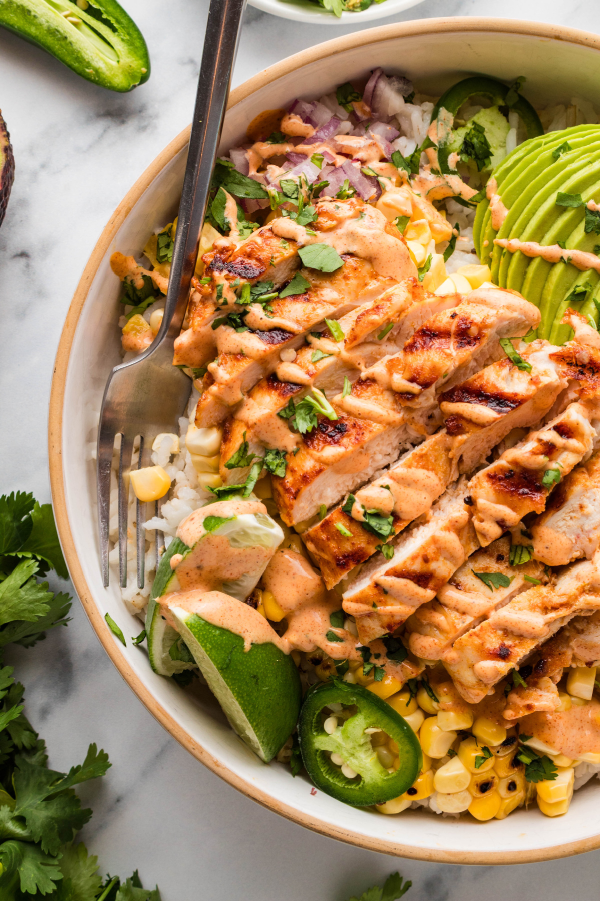 grilled chicken rice bowl with charred corn, avocado, lime wedge, jalape&ntilde;os, and creamy elote-style sauce