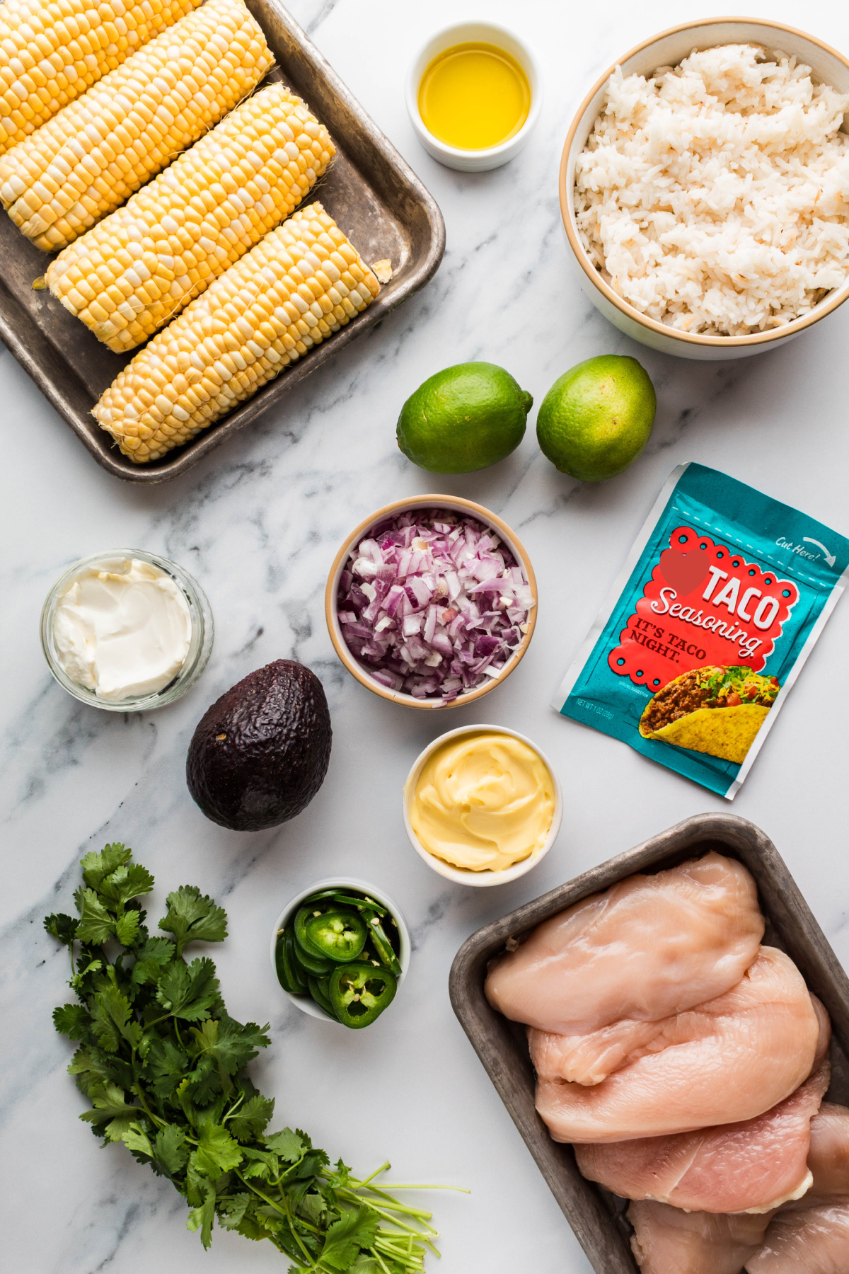 ingredients for chicken rice bowls including corn, rice, chicken breasts, avocado, lime, red onion, jalape&ntilde;os, mayonnaise, and taco seasoning
