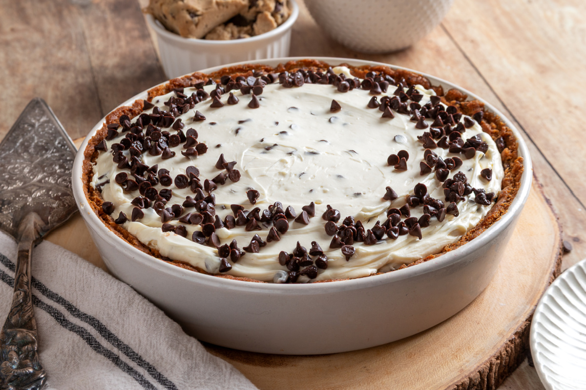 Chocolate chip cookie dough crust cheesecake in a round baking dish with creamy no-bake filling and mini chocolate chips