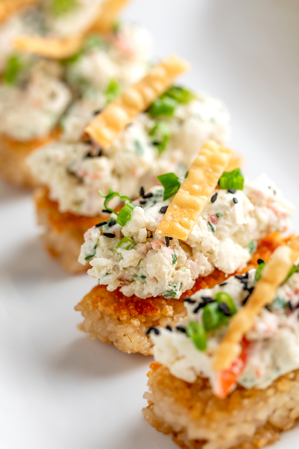 Crispy Rice Crab Rangoon Bites lined up with creamy crab topping, green onions, sesame seeds, and wonton strips