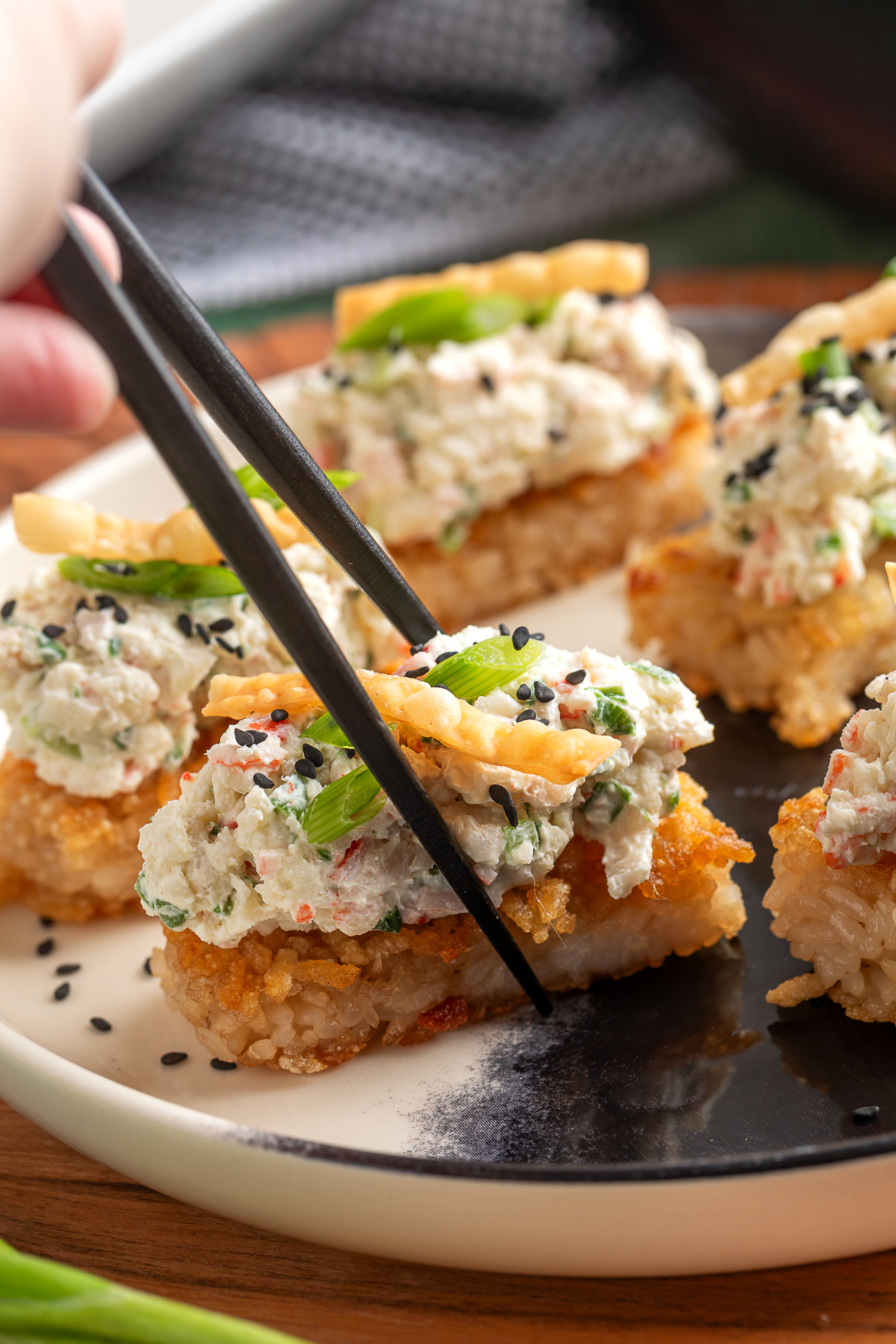 Crispy Rice Crab Rangoon Bites being picked up with chopsticks showing creamy crab topping and crispy rice base